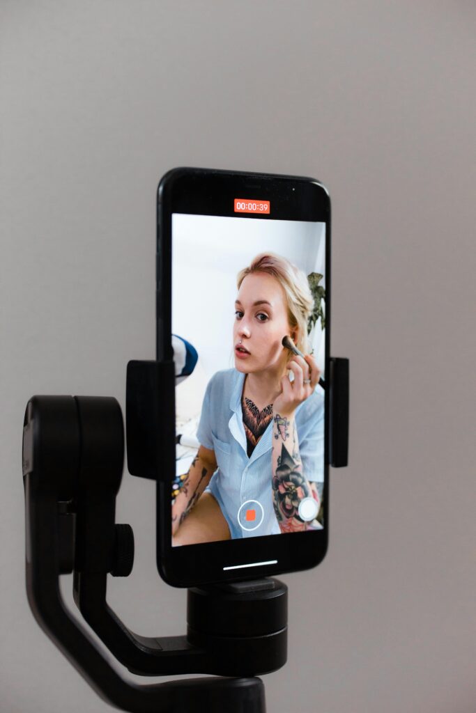 A woman records a makeup tutorial using a smartphone on a gimbal, capturing content for social media.